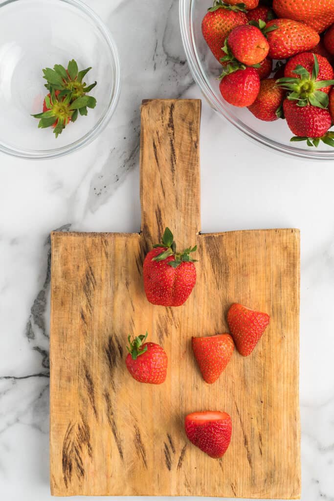 Prepping fresh strawberries sitting on a cutting board.
