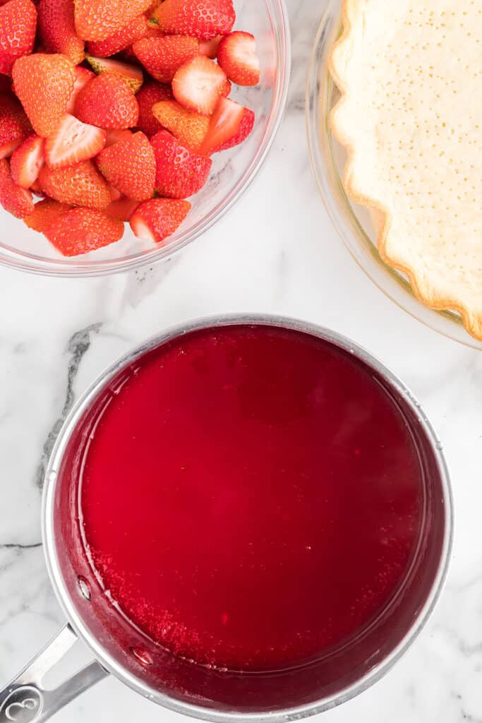 Strawberry jello added to sugar-water mixture in saucepan.