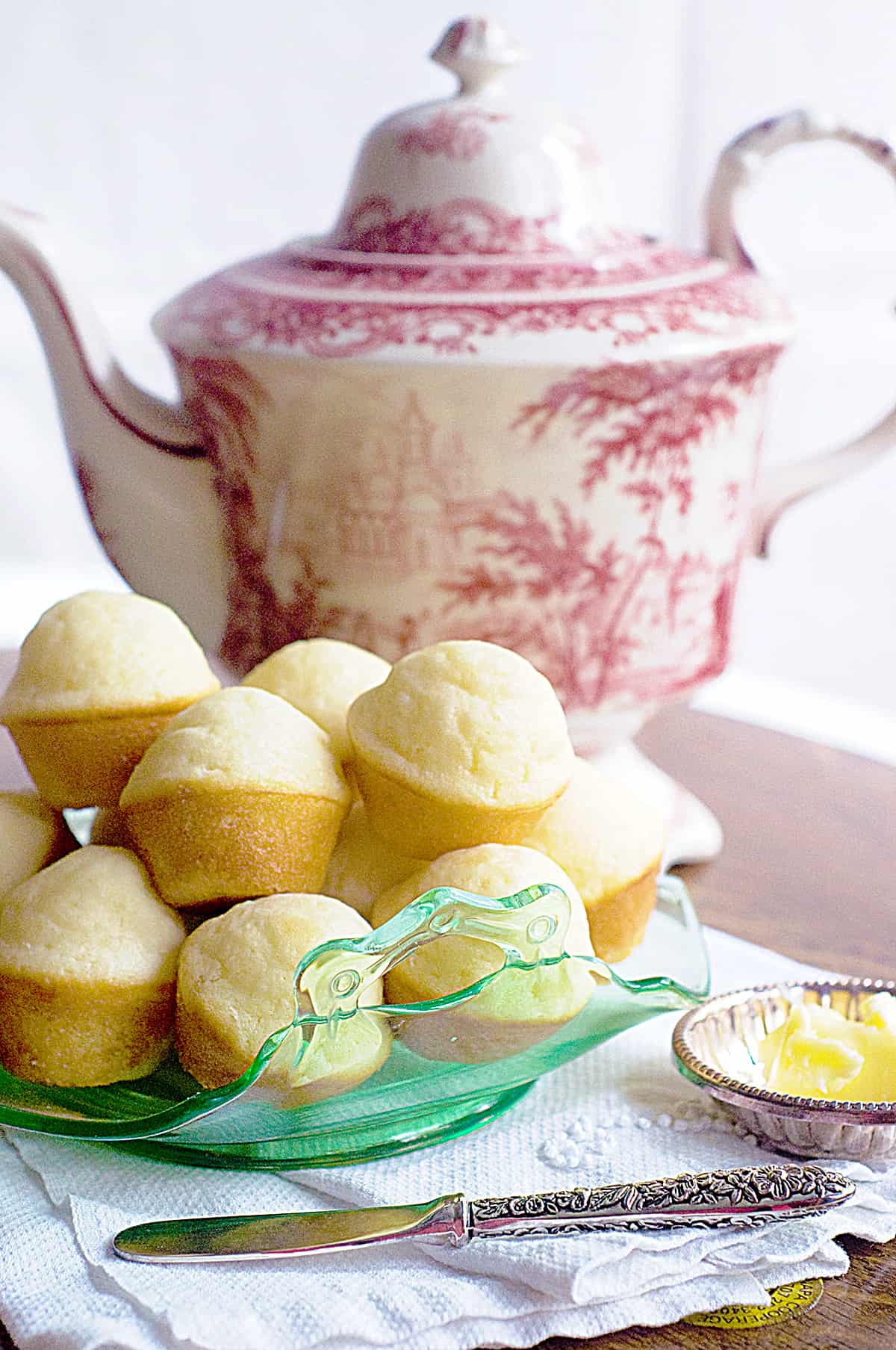Tea muffins piled high on a serving plate with a pot of tea in the background.