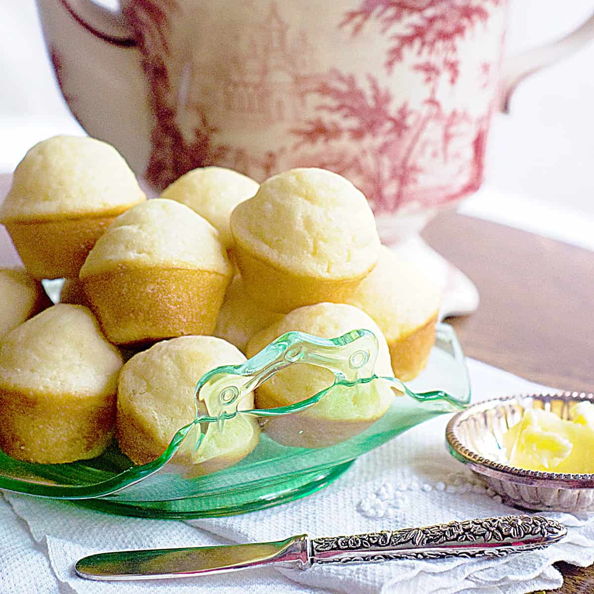 Tea muffins piled high on a serving plate with a pot of tea in the background.