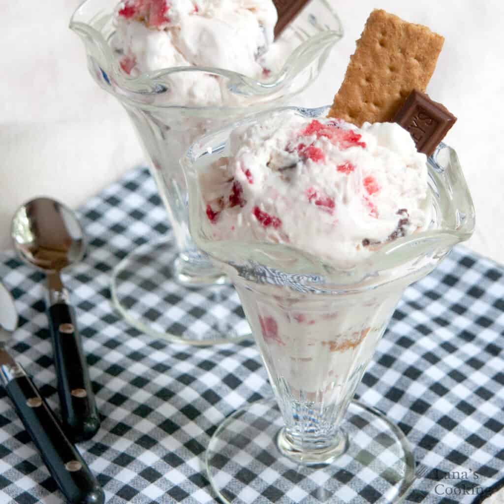 Two glass sundae dishes filled with ice cream, chocolate, and graham crackers on a checkered cloth.