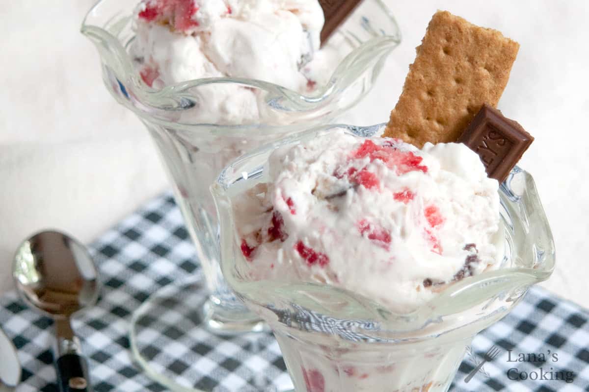 Two glass dishes of ice cream with chocolate pieces and graham crackers on a checkered cloth.