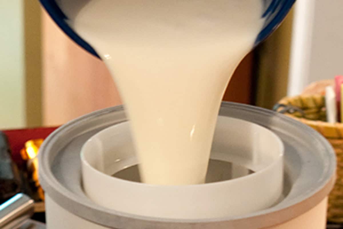 Thick white liquid being poured into an ice cream maker.