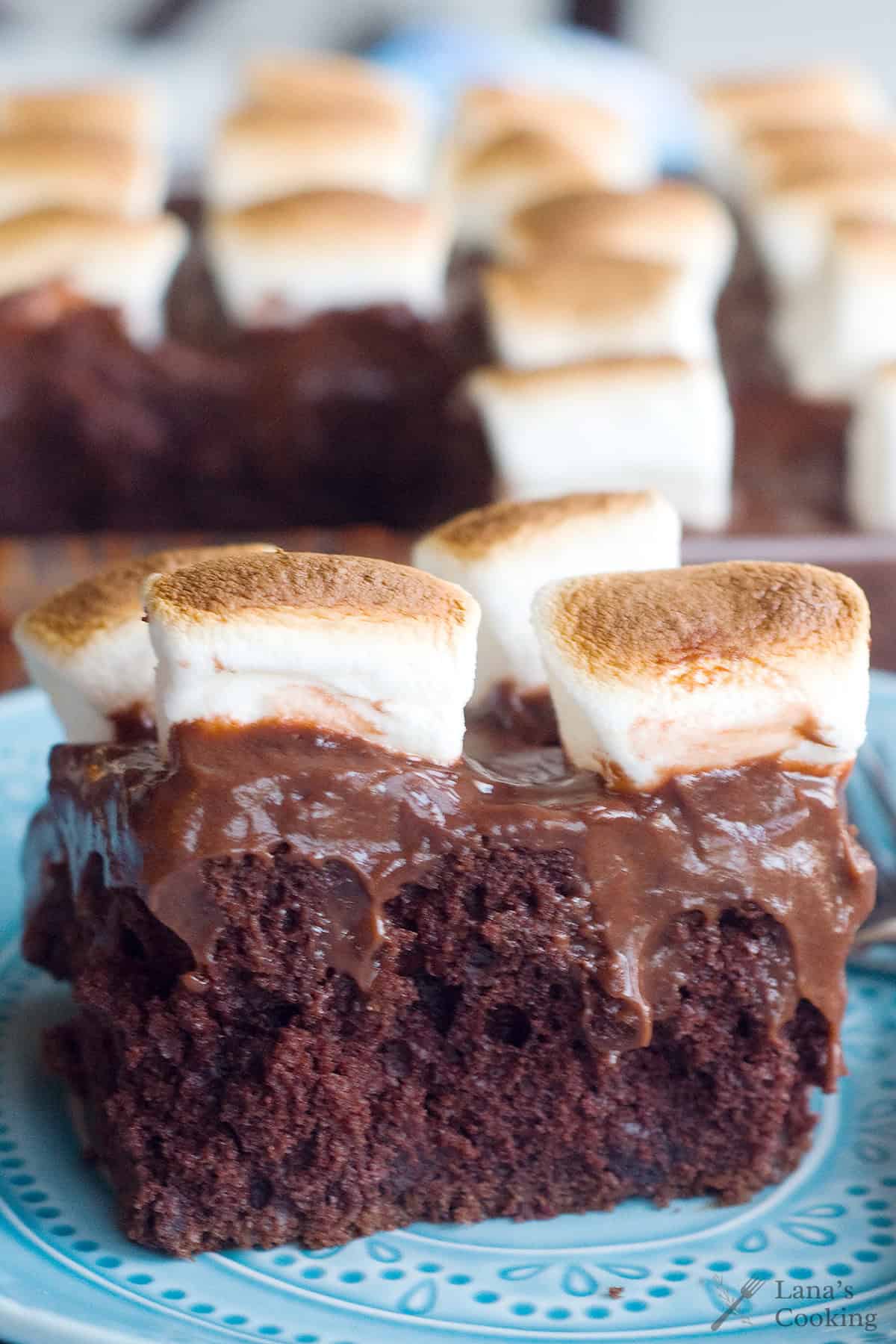 A slice of chocolate cake topped with chocolate pudding and toasted marshmallows on a blue patterned plate.