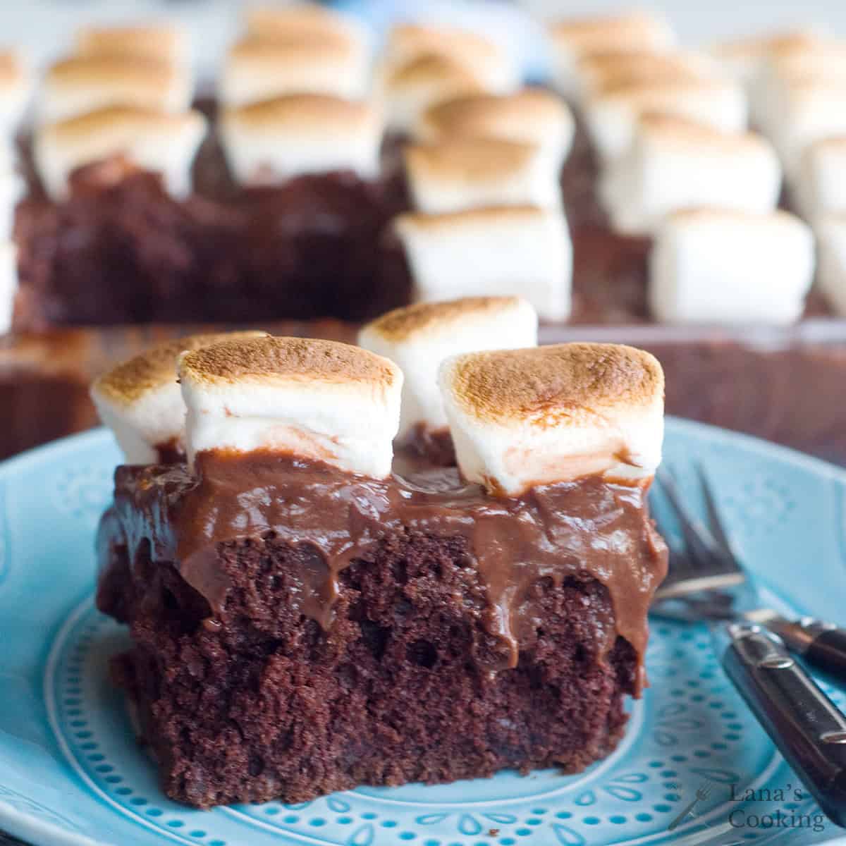 A slice of chocolate poke cake topped with chocolate pudding and toasted marshmallows on a blue plate with a fork.