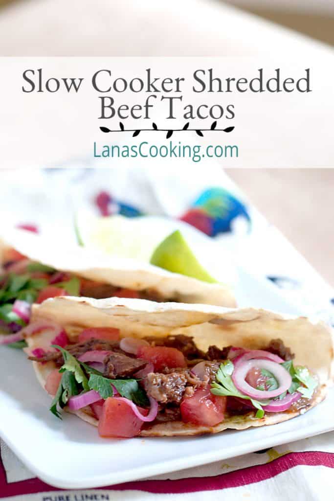 Two slow cooker shredded beef tacos on a serving plate with a kitchen towel underneath. Text overlay for pinning.