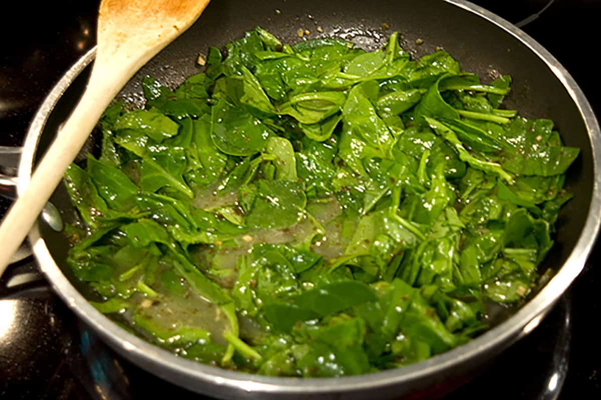 Fresh spinach leaves stirred into the egg white mixture, with a wooden spoon resting on the side.