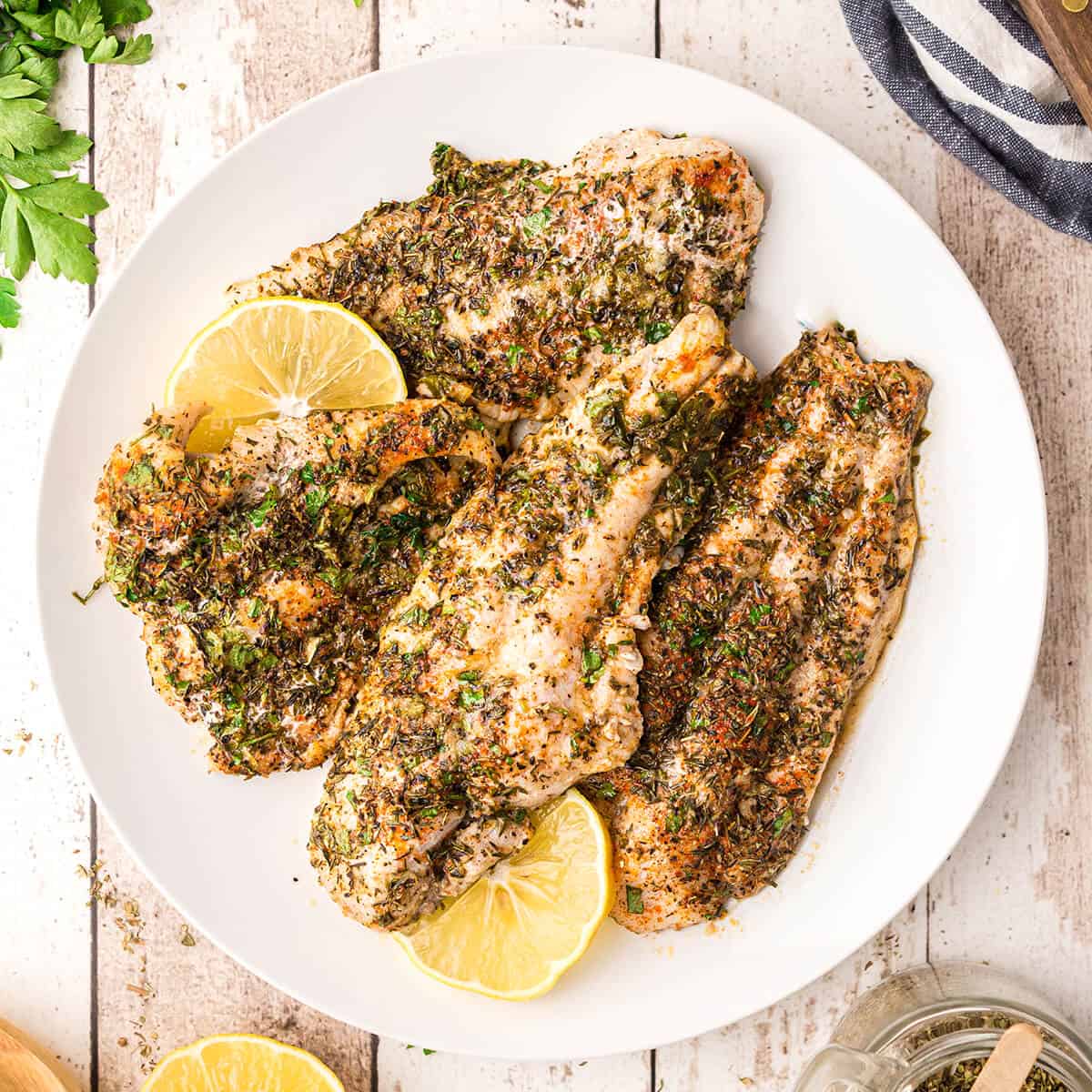 Baked catfish with lemon slices on a white serving plate.