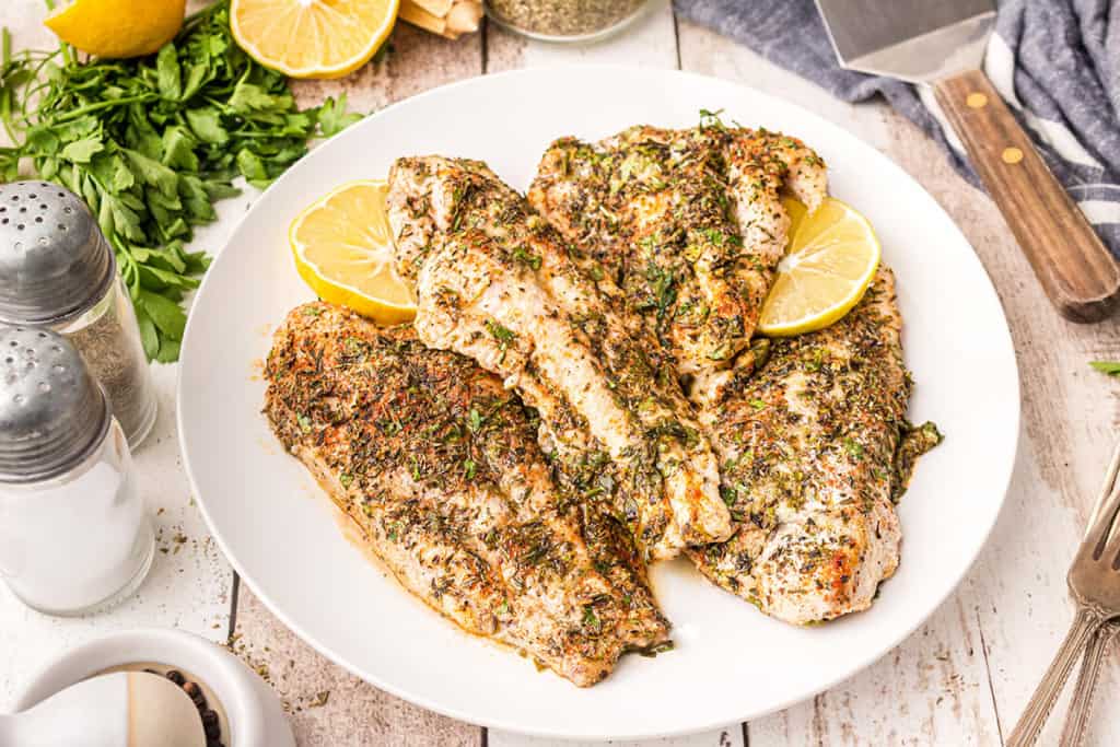 Baked catfish with lemon slices on a white serving plate.