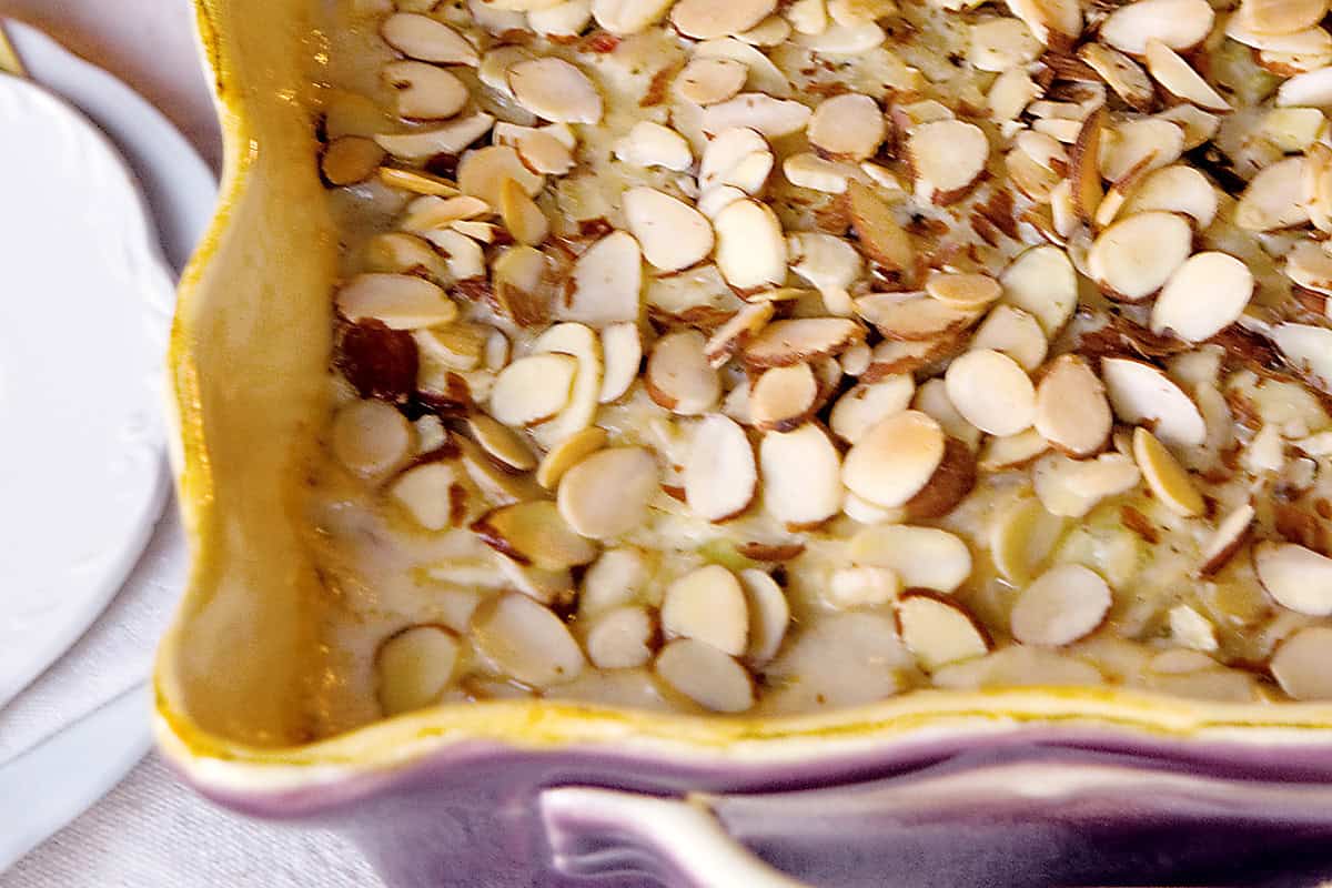 A baked casserole topped with sliced almonds in a purple and yellow dish.