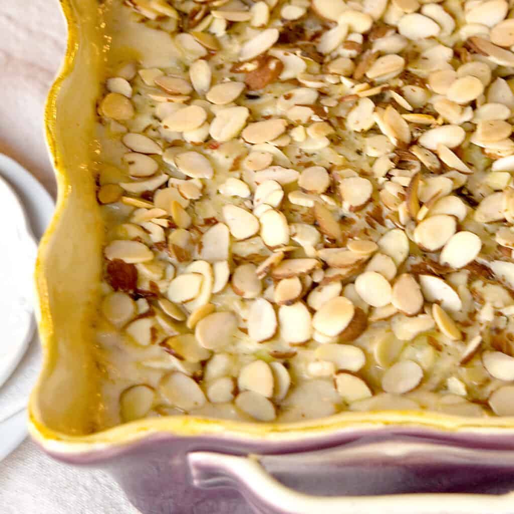 A close-up of a baked casserole topped with sliced almonds in a yellow-edged ceramic dish.