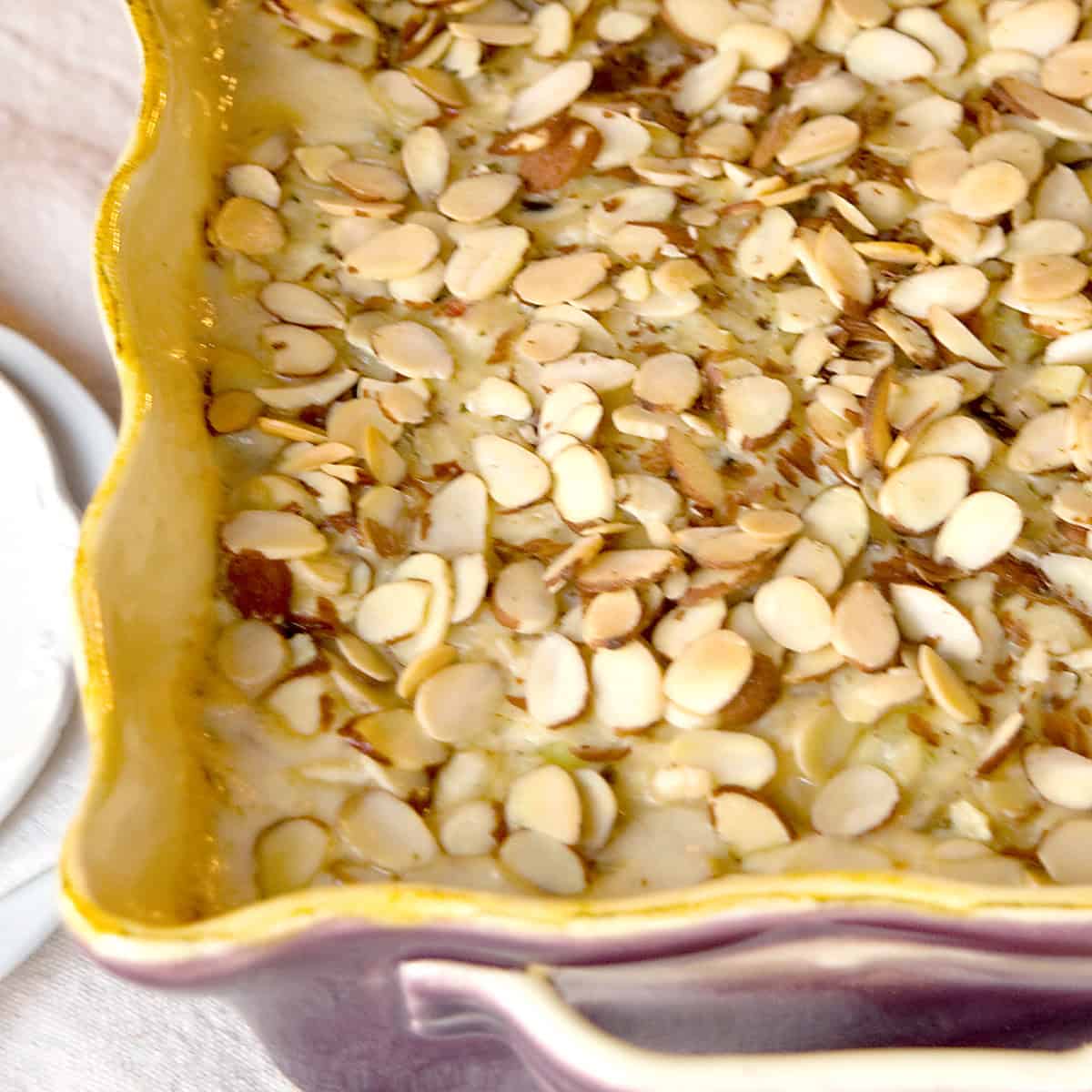 A close-up of a baked casserole topped with sliced almonds in a yellow-edged ceramic dish.
