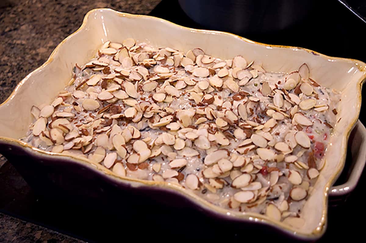 A casserole dish filled with creamy mixture topped with sliced almonds, ready to be baked.