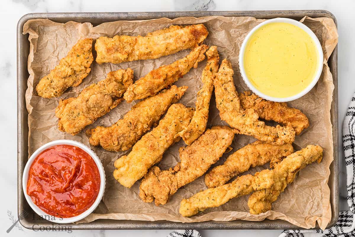 Finished fried chicken fingers with dipping sauces on the side.