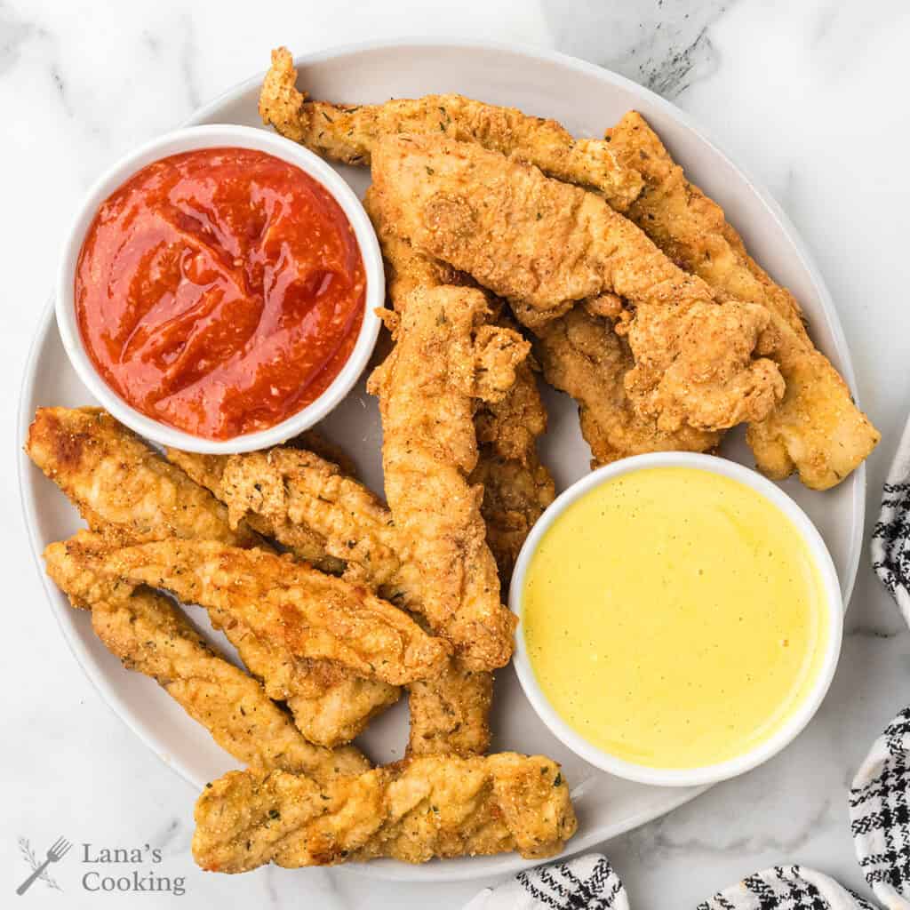 Finished fried chicken fingers with dipping sauces on the side.