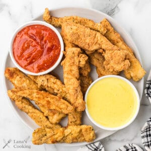 Finished fried chicken fingers with dipping sauces on the side.