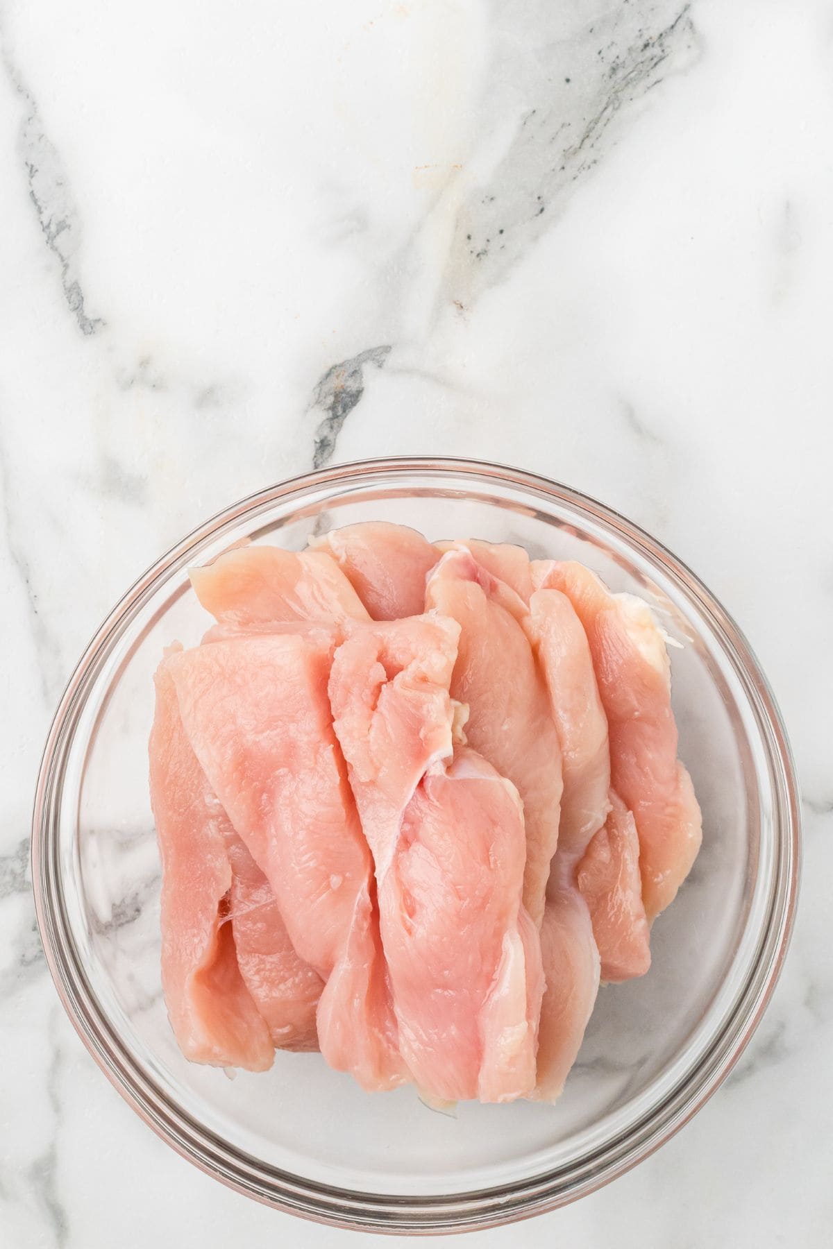 Chicken breast strips in a glass bowl.