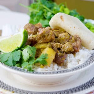 A plate of rice topped with meat stew, garnished with cilantro, lime, and a folded tortilla.