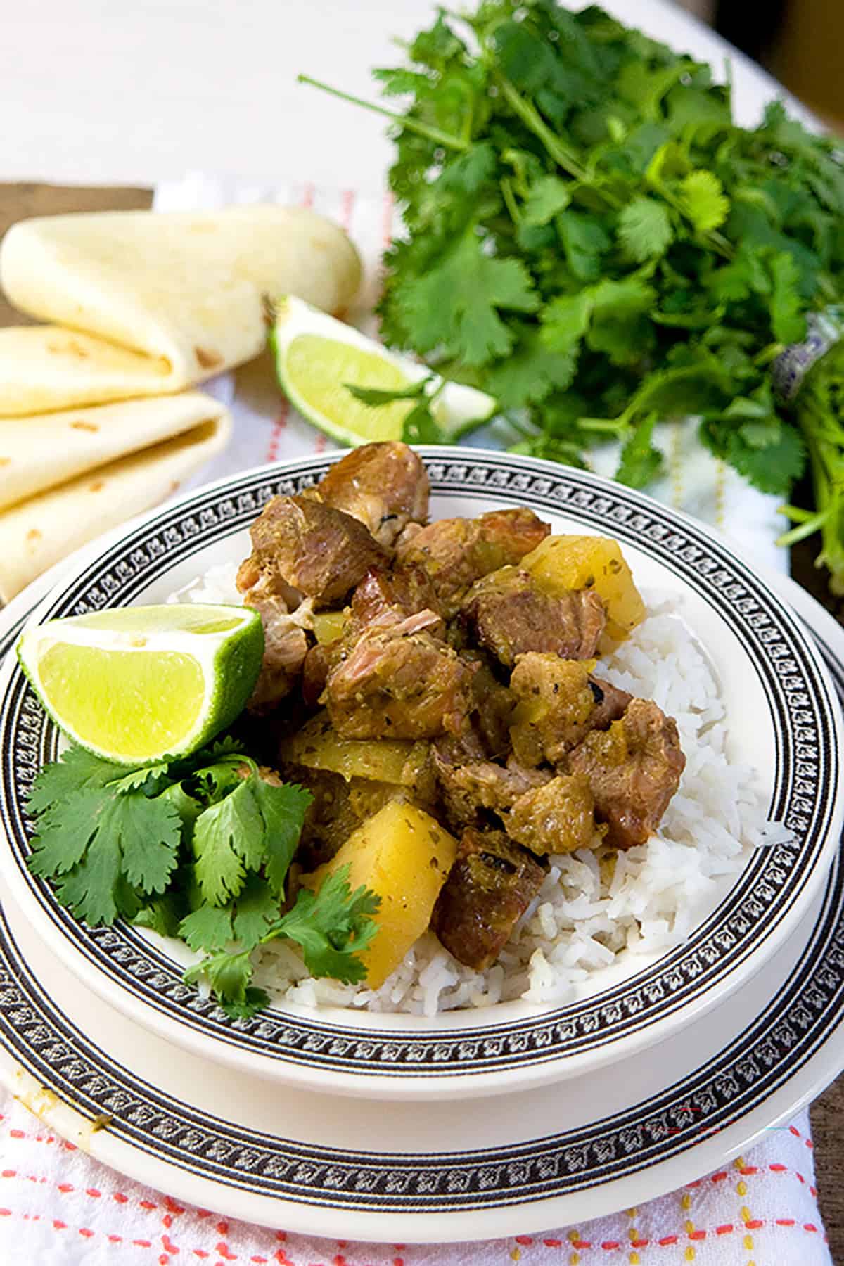A plate of rice topped with meat and potatoes, garnished with lime and cilantro, next to flatbread and herbs.
