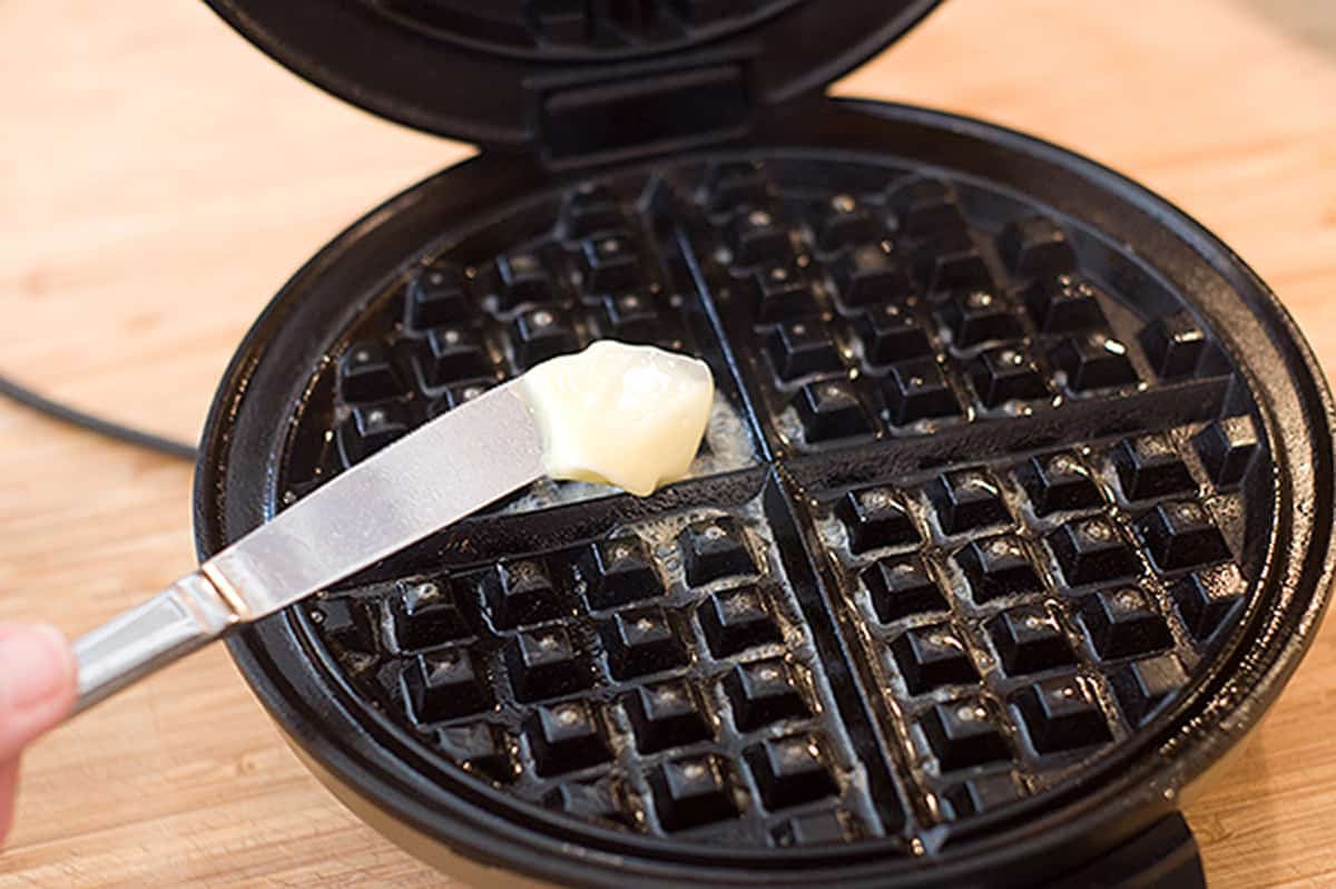 Adding butter to heated waffle iron.