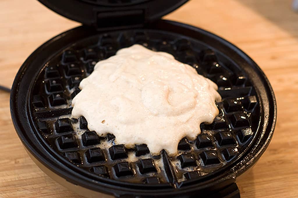 A waffle iron with waffle batter on top.