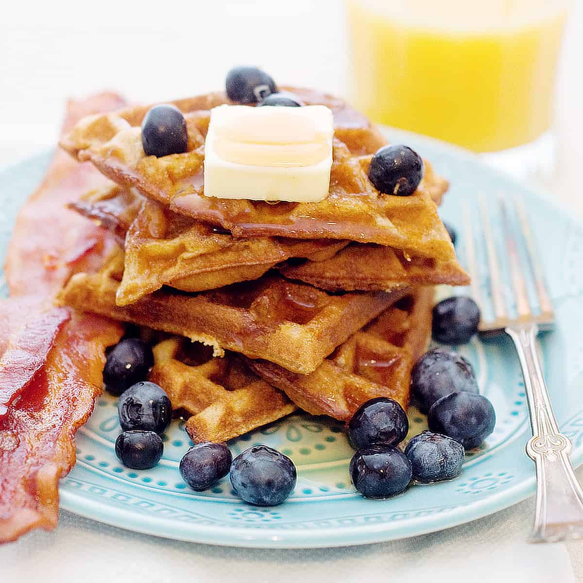 A stack of cinnamon and brown sugar waffles with fresh blueberries and syrup.