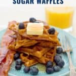 Stack of waffles with butter and blueberries, served with bacon and orange juice on a blue plate.