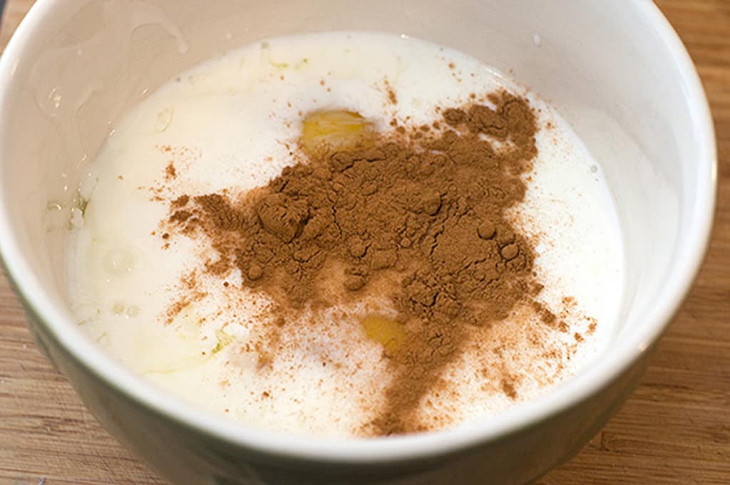 A bowl with milk a cracked egg, and a heap of cinnamon powder on top.