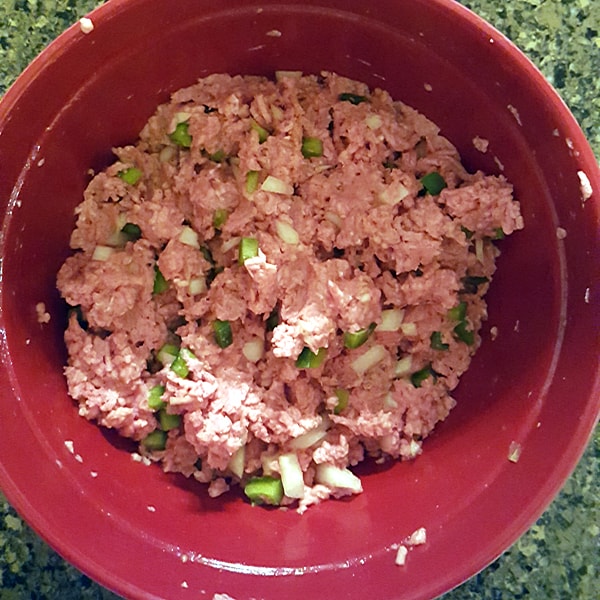 Burger mixture of beef, pork, onions, peppers, egg, and bread crumbs in a mixing bowl.