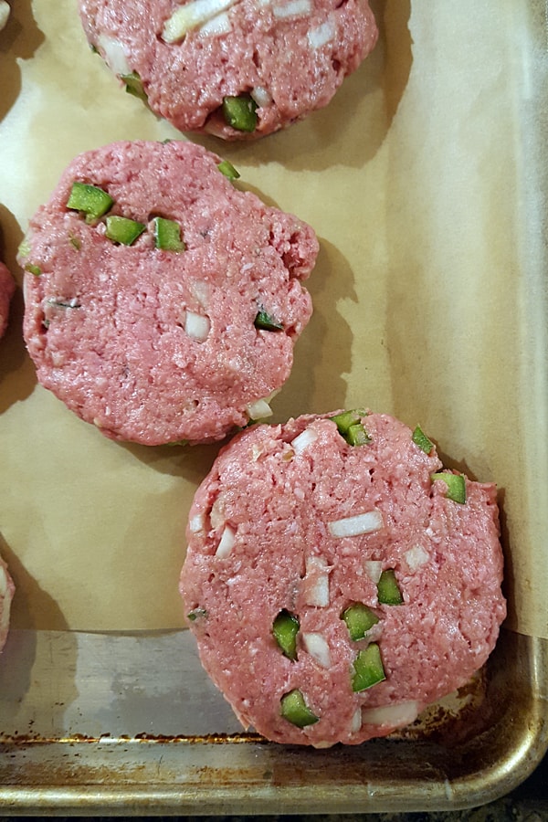 Burger patties on a parchment lined baking sheet.
