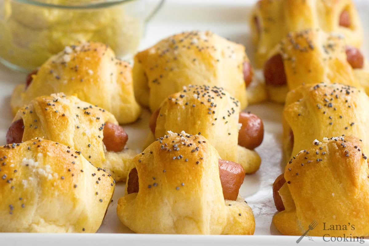 Sausage Pineapple Rollups topped with poppy seeds on a white tray, with a bowl of mustard in the background.