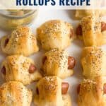 Baked sausage pineapple rollups topped with seasoning, served with dipping sauce on a white surface.