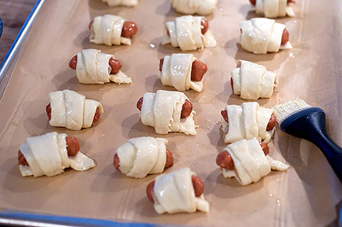 Unbaked rollups on a baking sheet with a pastry brush nearby.