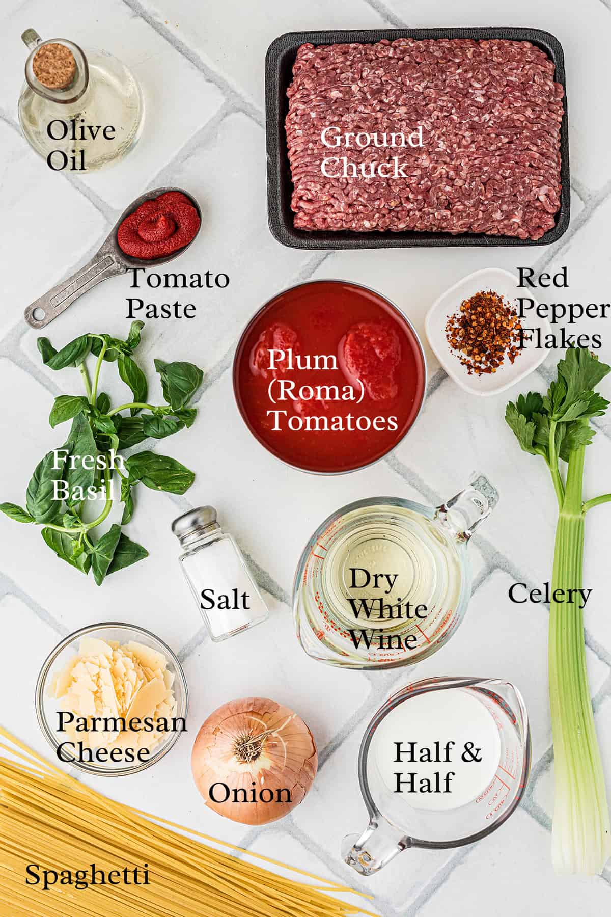 Ingredients for traditional Bolognese sauce arranged on a counter, including ground chuck, tomato paste, plum tomatoes, onion, celery, dry white wine, half & half, cheese, basil, and seasonings.