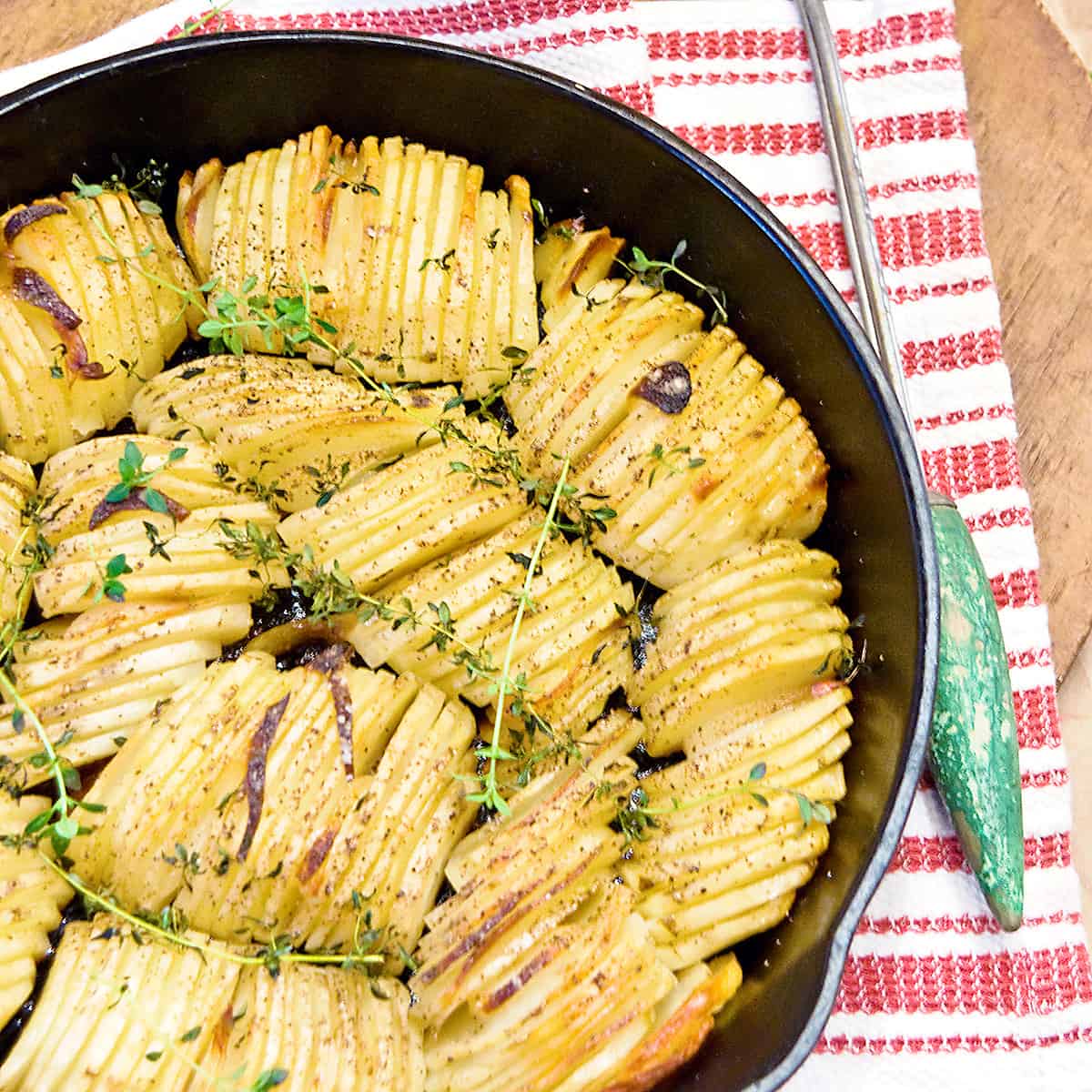 Crispy roasted potatoes in a black cast iron skillet set on a kitchen towel with a serving fork alongside.