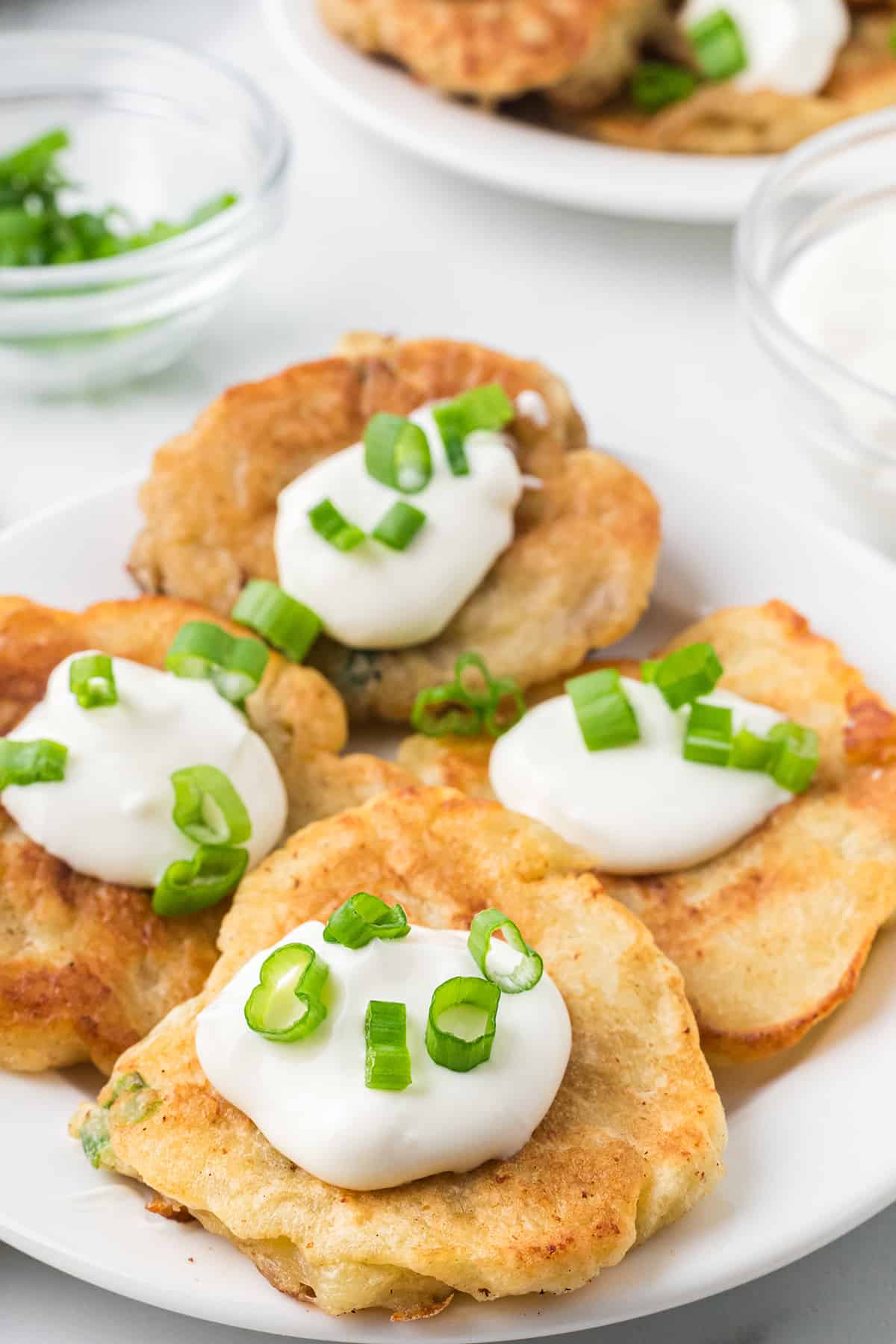 Boxty topped with sour cream and green onions on a white serving plate.