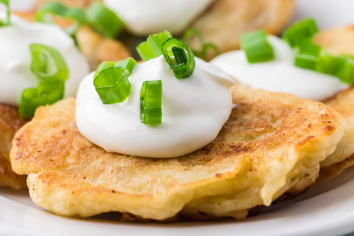 Boxty topped with sour cream and green onions on a plate.