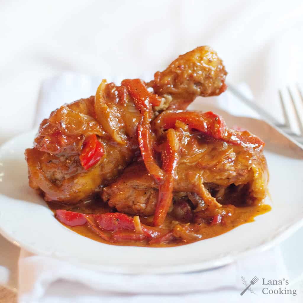 Paprika chicken with onions and red peppers in a rich sauce, served on a white plate with a fork in the background.