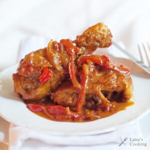Paprika chicken with onions and red peppers in a rich sauce, served on a white plate with a fork in the background.