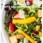 Close-up of a fresh salad with strawberries, mango, greens, croutons, and shaved cheese in a white bowl.