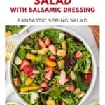 A bowl of strawberry salad with greens, croutons, carrots, cheese, and balsamic dressing.