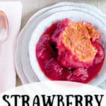 A serving of strawberry cobbler in a china dish with a spoon and napkin alongside.
