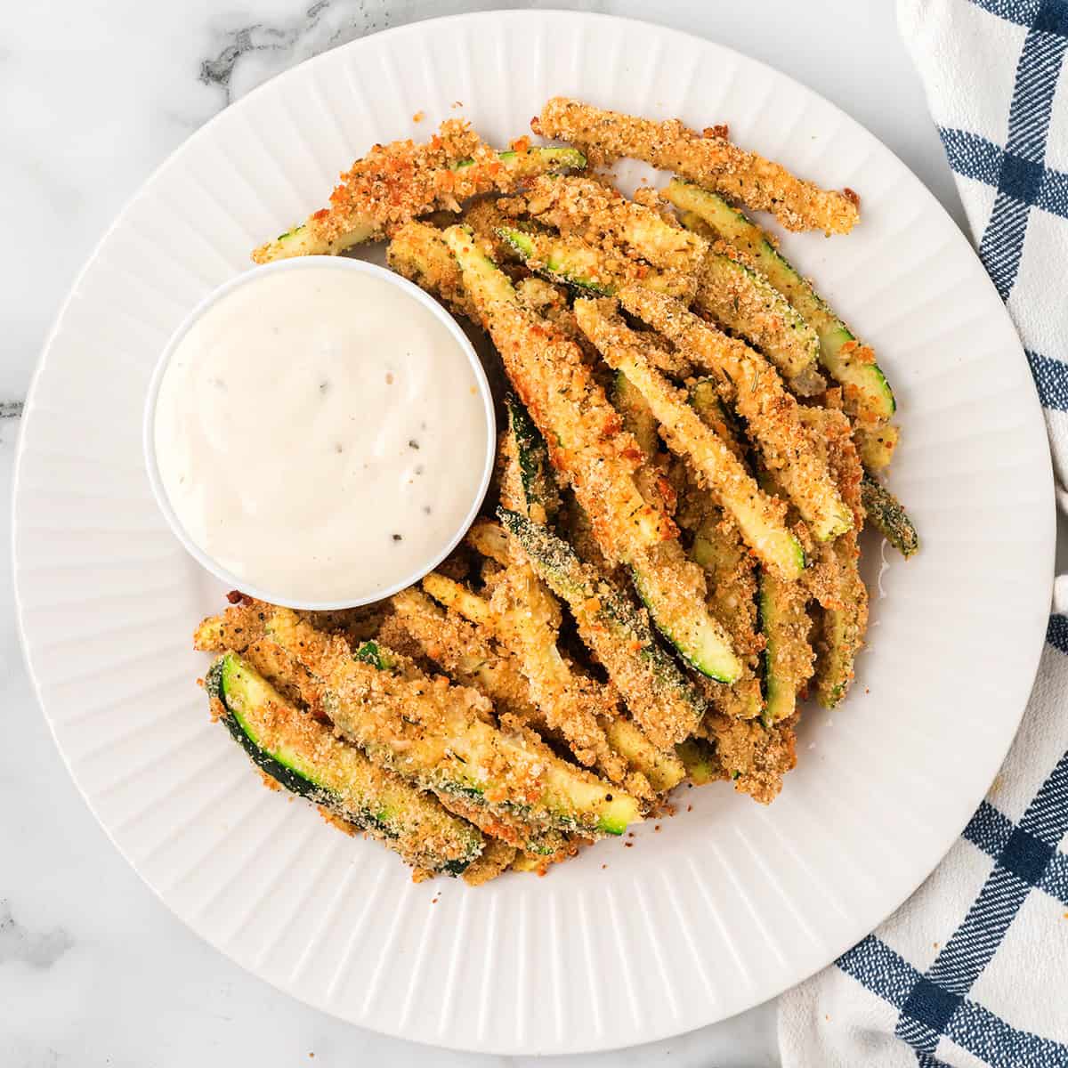 A plate filled with zucchini fries with dip on the side.