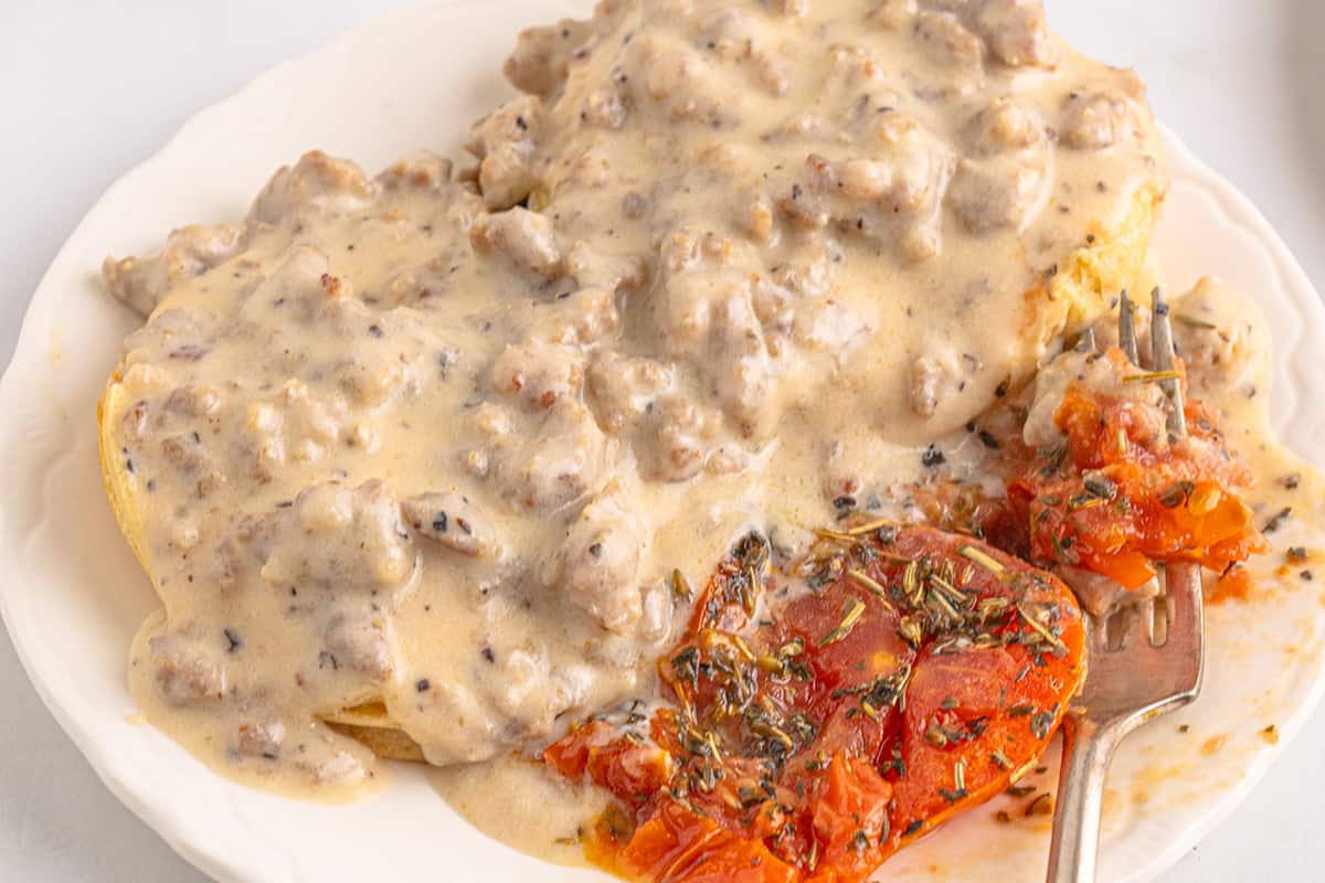Sausage gravy and biscuits on a plate with baked tomatoes.