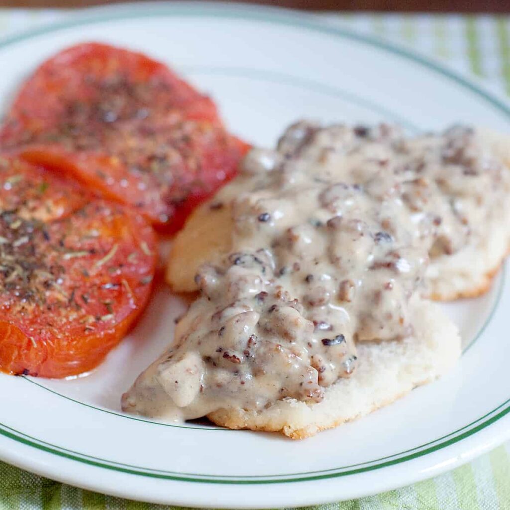 Sausage Gravy and Biscuits with Tomatoes - A hearty country breakfast of sausage gravy served over biscuits with baked, herbed tomato slices on the side. https://www.lanascooking.com/sausage-gravy-and-biscuits-with-tomatoes/