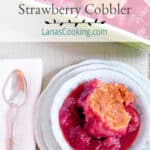 A serving of strawberry cobbler in a china dish with a spoon and napkin alongside.
