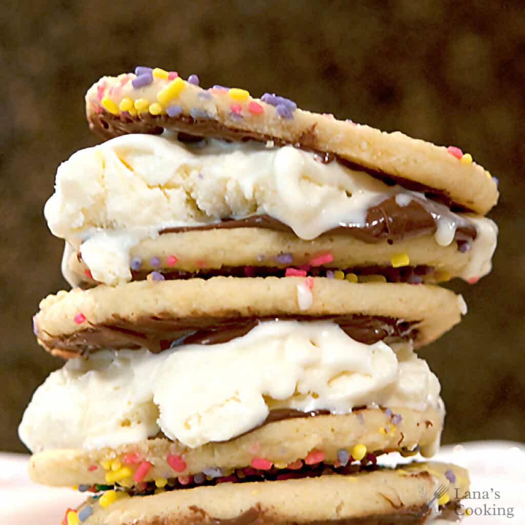 A stack of three ice cream sandwiches made with sprinkle-covered cookies, vanilla ice cream, and a layer of Nutella spread.