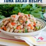 A bowl of cannellini bean and tuna salad with vegetables, set in front of fresh parsley on a table.