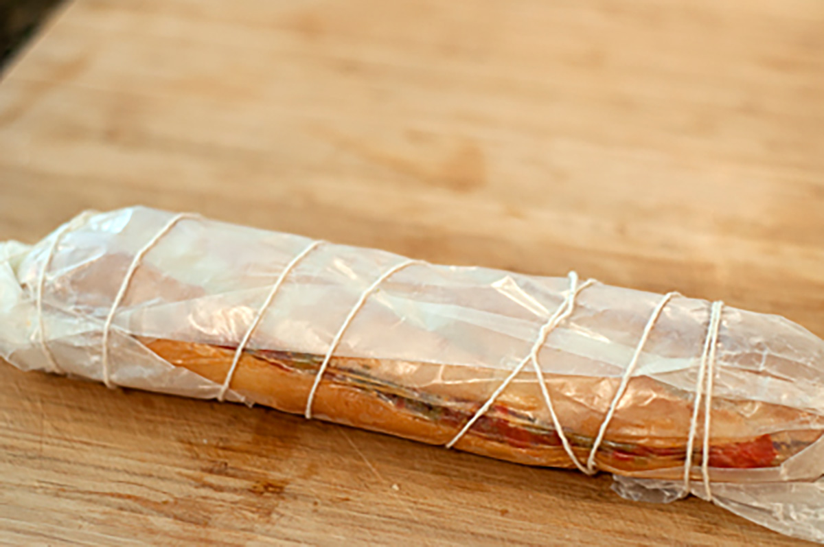 A sandwich wrapped in parchment paper and tied with string, placed on a wooden surface.