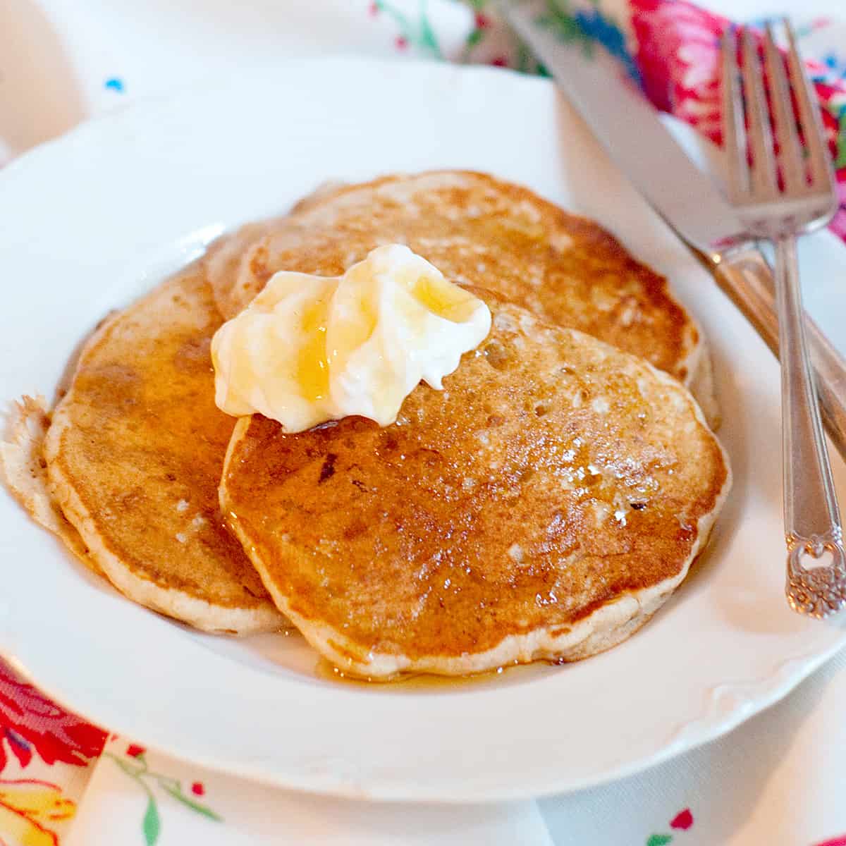 Finished pancakes topped with yogurt and syrup on a white serving plate.